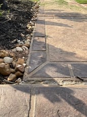 Stamped concrete A close up of a sidewalk with stamped concrete detailing that looks like stone. There are small rocks and plants surrounding the sidewalk.