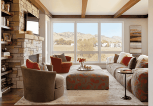 living room The inside of a living room with large windows on one wall, a fireplace and TV to the left, and a couch with two matching round chairs across from it with a matching patterned ottoman.