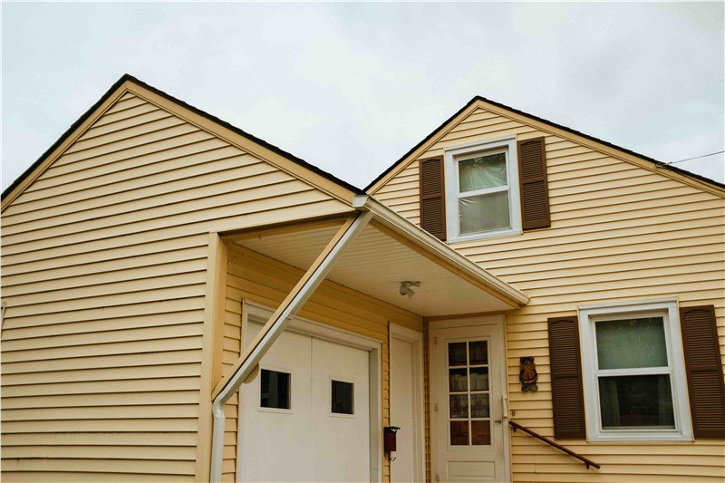The front of a house with yellow/orange lap siding and white trim with brown shutters around the windows.
