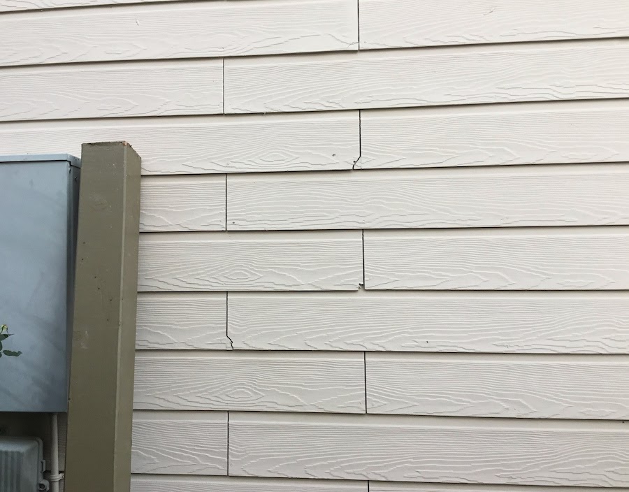 The side of a home with beige lap siding with some chipped panels at the corners.