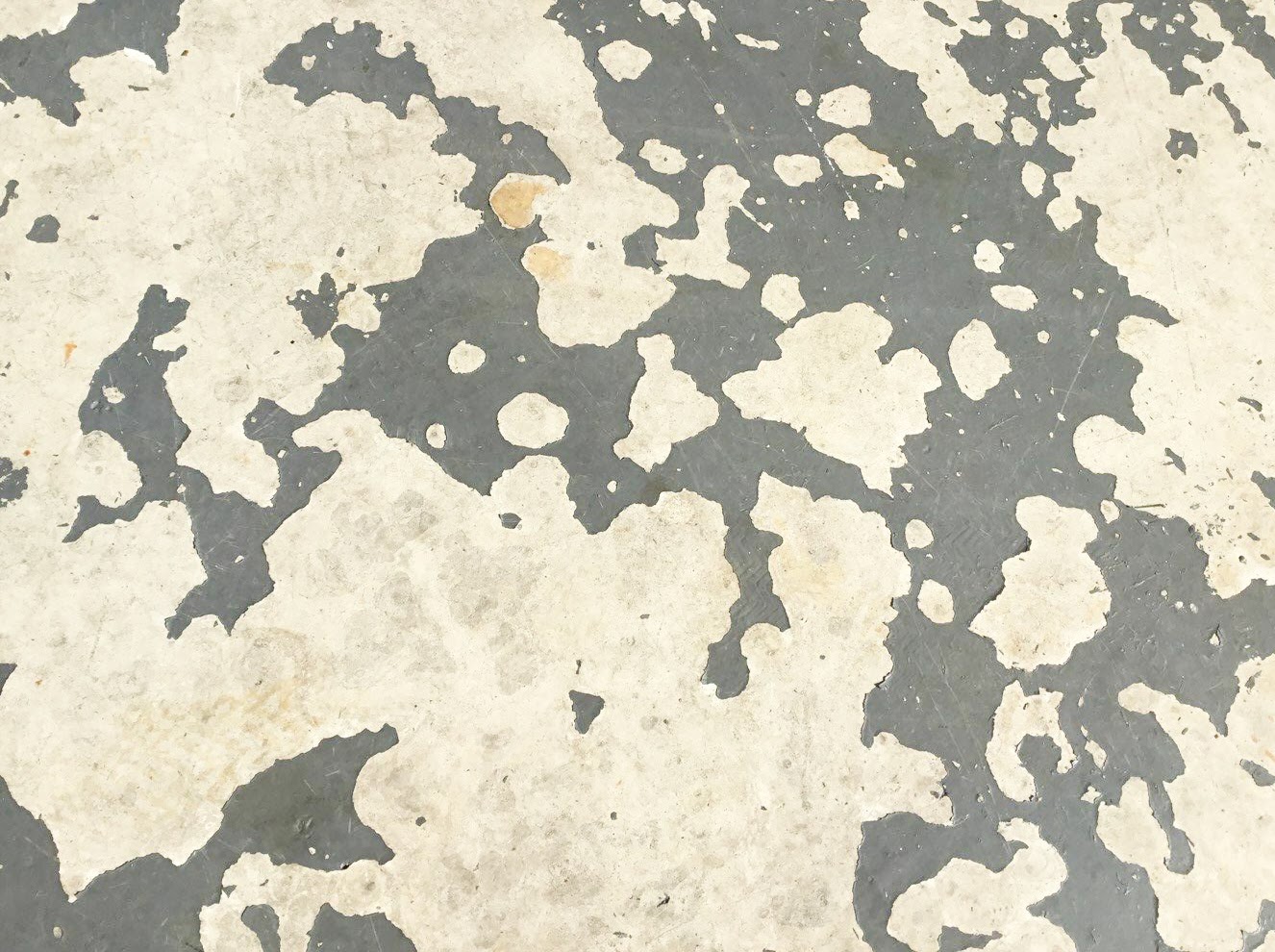 A close up of a concrete floor with a grey coating that is chipping and peeling to white.