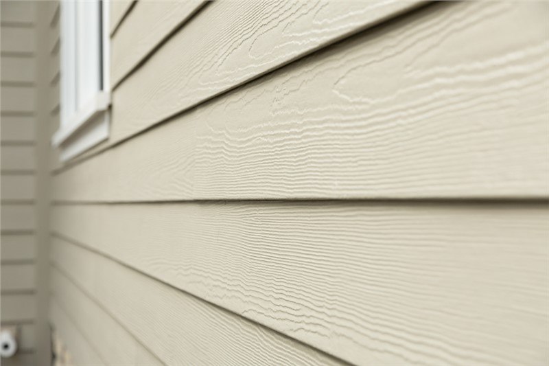 A close shot of the side of a home at an angle. The horizontal lap siding is a beige color with a cedar finish.