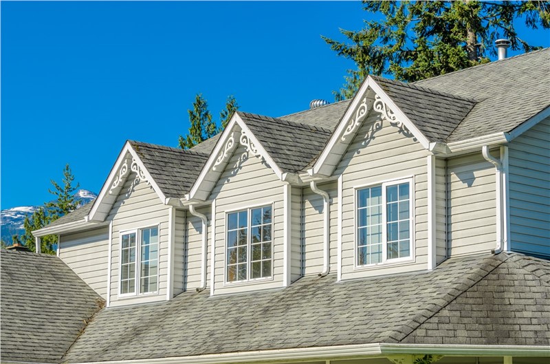 A close up of the top half of a home with three gables with white windows with gridding. The siding is a light beige.