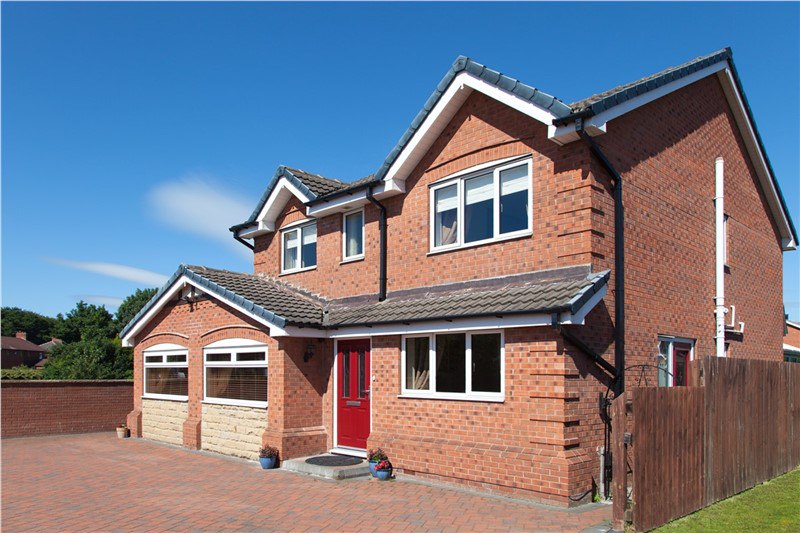 A home with red brick and white windows with a blue sky in the background. The home has a red door. 